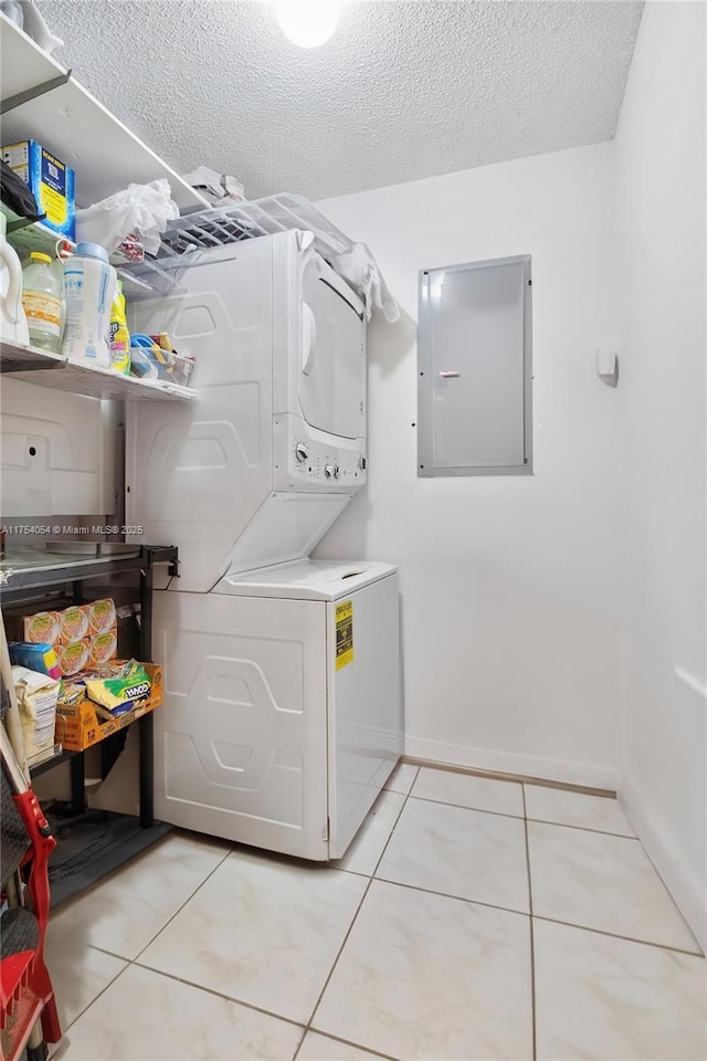 laundry area featuring stacked washer and dryer, laundry area, electric panel, light tile patterned floors, and a textured ceiling