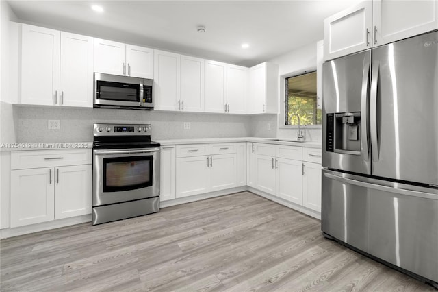 kitchen with light wood-style flooring, a sink, white cabinets, light countertops, and appliances with stainless steel finishes