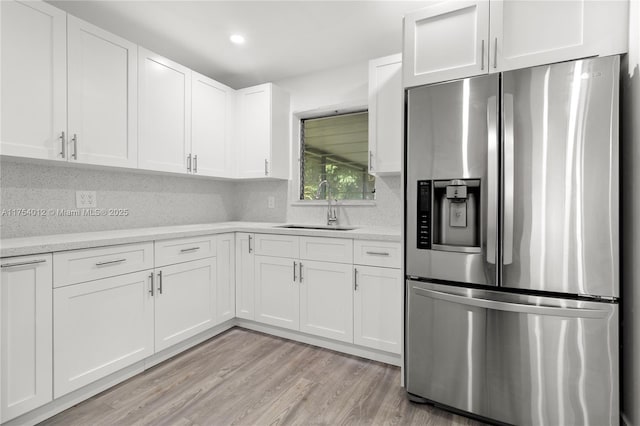 kitchen with stainless steel fridge, white cabinets, a sink, light wood-style floors, and backsplash