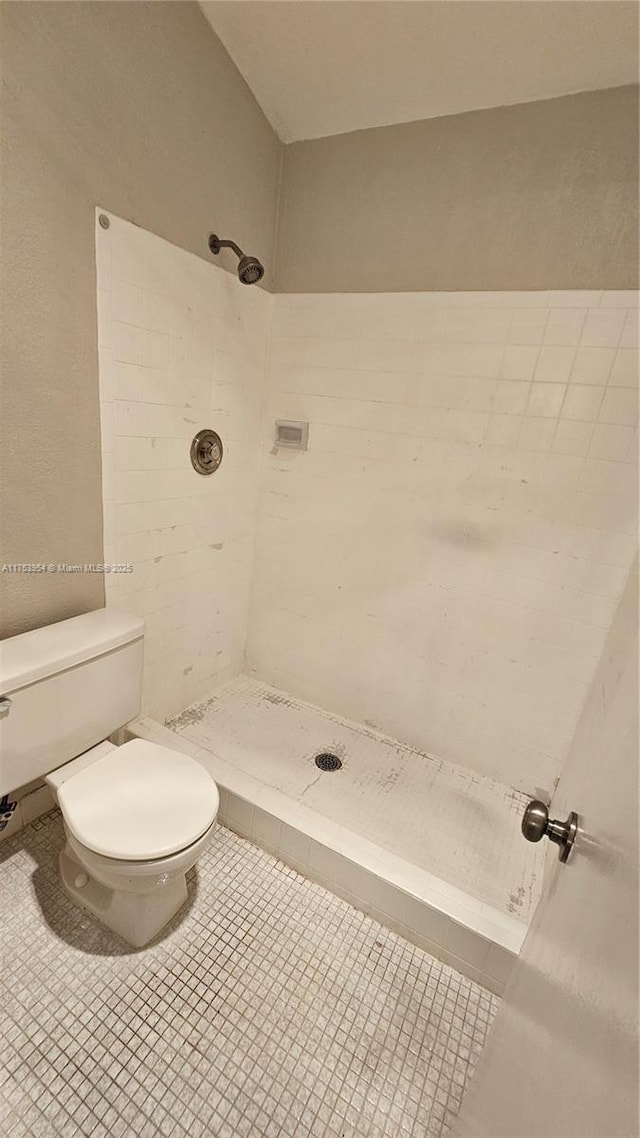 bathroom featuring tile patterned flooring, tiled shower, and toilet