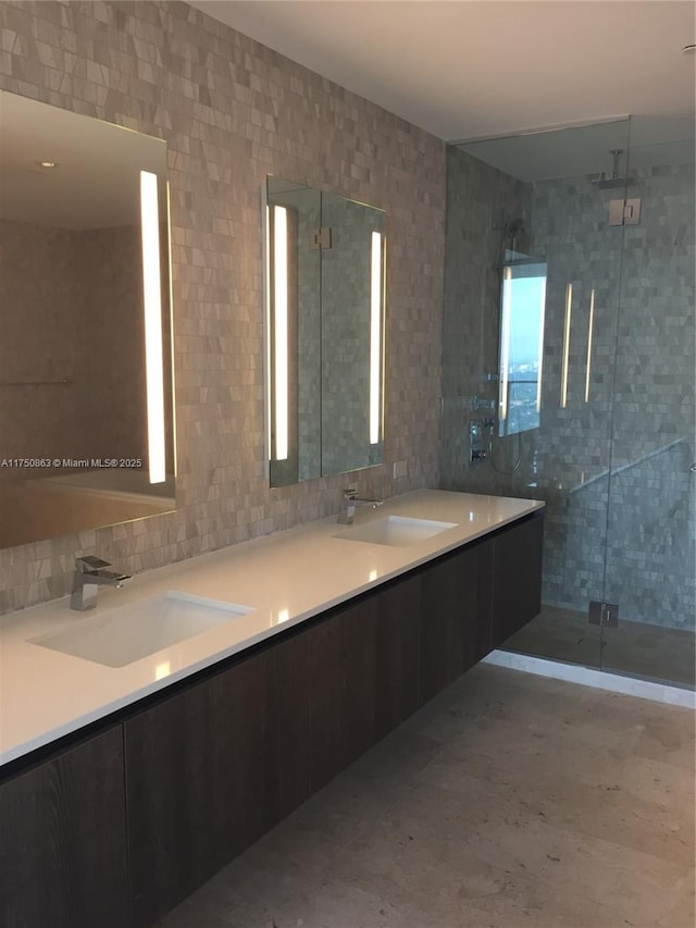 full bathroom featuring double vanity, a stall shower, decorative backsplash, and a sink