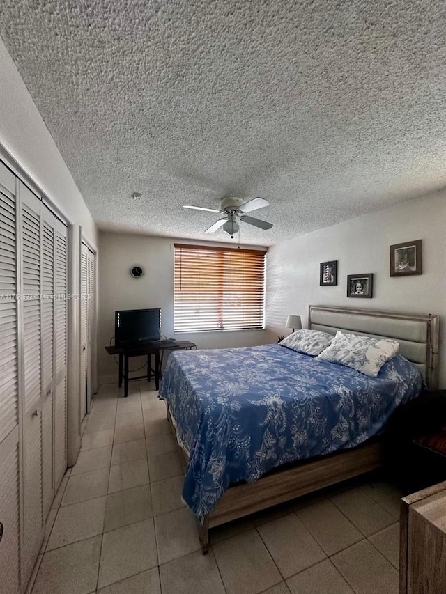 bedroom featuring light tile patterned floors, ceiling fan, a textured ceiling, and multiple closets