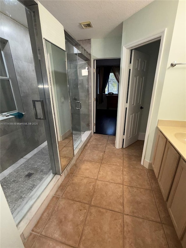 full bathroom featuring a textured ceiling, tile patterned flooring, vanity, visible vents, and a shower stall