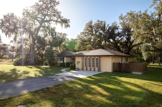 ranch-style house with driveway, fence, a front lawn, and stucco siding