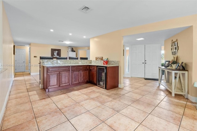 kitchen featuring light tile patterned floors, wine cooler, a peninsula, visible vents, and light stone countertops