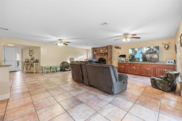 living area featuring light tile patterned floors, baseboards, visible vents, a ceiling fan, and a fireplace