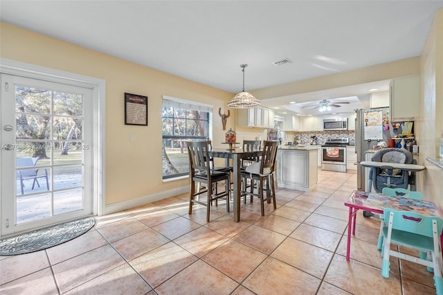 dining area with a ceiling fan, light tile patterned flooring, visible vents, and baseboards