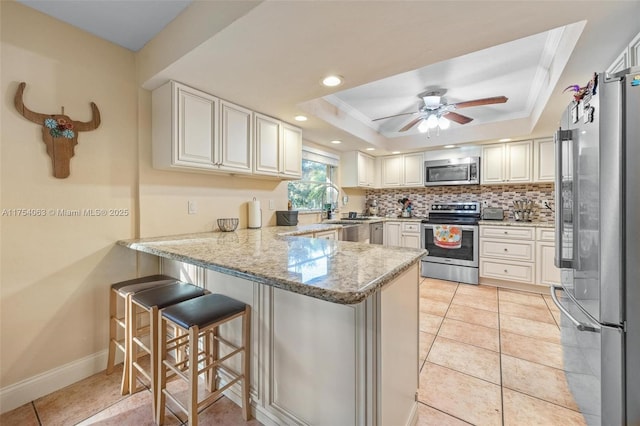 kitchen with a raised ceiling, backsplash, a peninsula, stainless steel appliances, and a sink