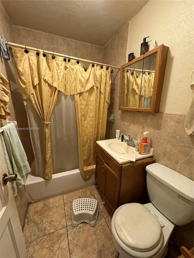 full bath featuring toilet, tile patterned floors, shower / bath combo with shower curtain, vanity, and tile walls