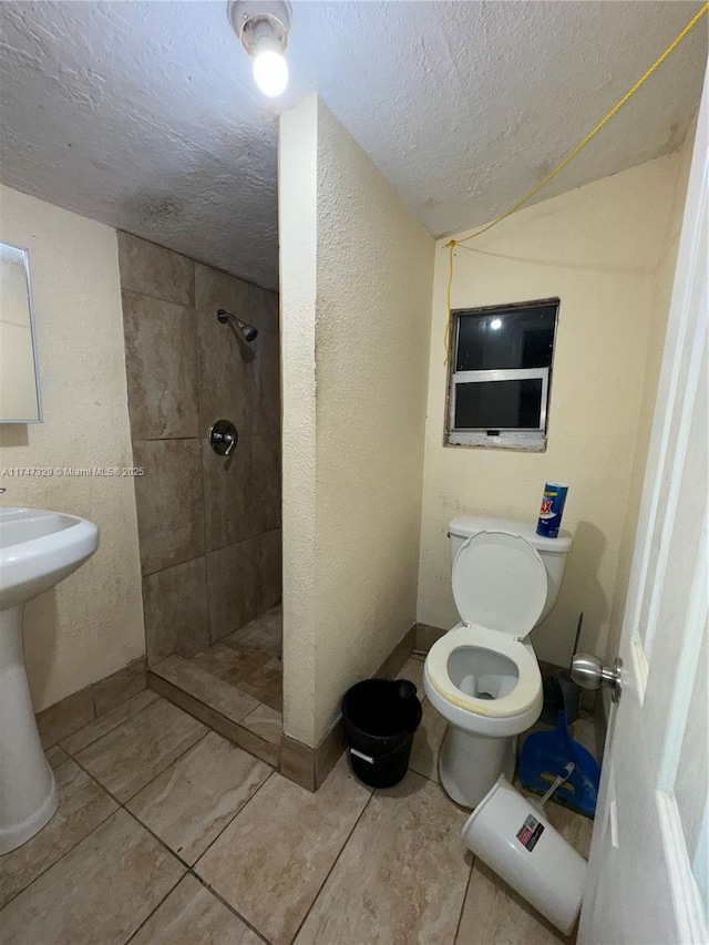 bathroom with a textured wall, toilet, a sink, a textured ceiling, and tiled shower