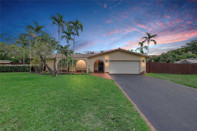 view of front of house featuring driveway, an attached garage, fence, a front yard, and stucco siding