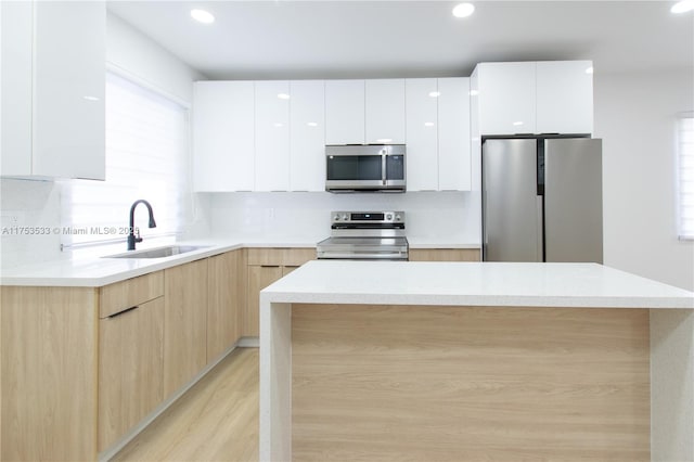 kitchen with stainless steel appliances, light brown cabinetry, modern cabinets, and a sink