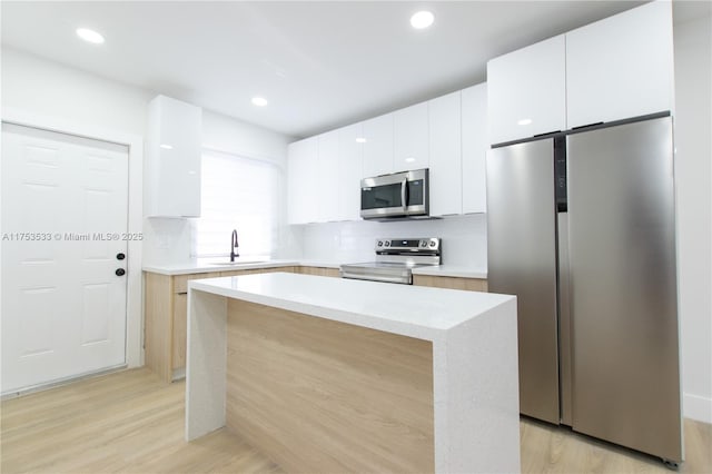 kitchen featuring appliances with stainless steel finishes, a sink, light wood-style floors, and a center island