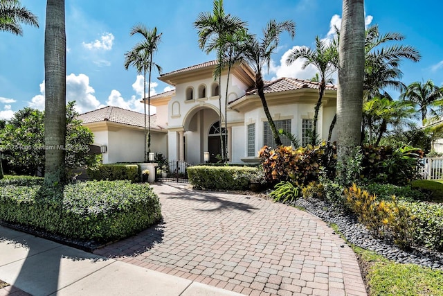 mediterranean / spanish home with a tile roof, stucco siding, and fence