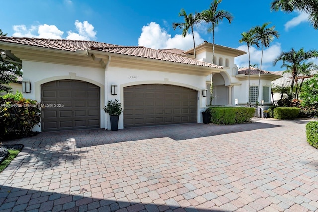 mediterranean / spanish home with driveway, a tile roof, a garage, and stucco siding