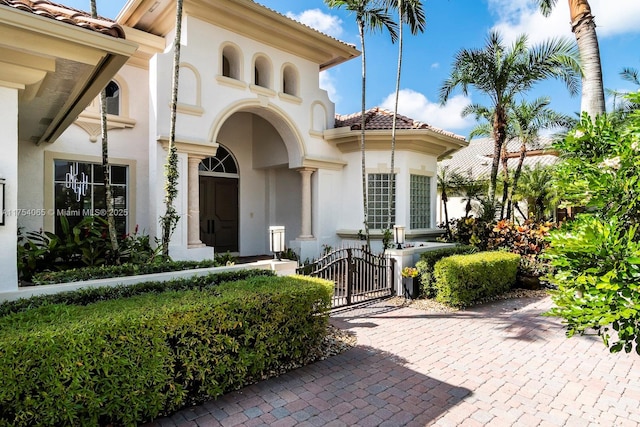 doorway to property featuring a tiled roof, a gate, and stucco siding