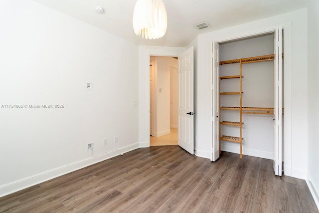 unfurnished bedroom with baseboards, visible vents, wood finished floors, and a closet