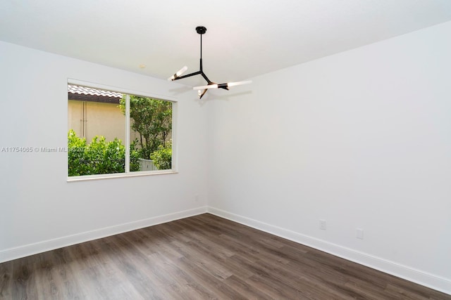 spare room with baseboards, a chandelier, and dark wood finished floors