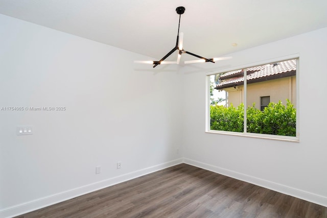 spare room with dark wood-style floors, baseboards, and a chandelier