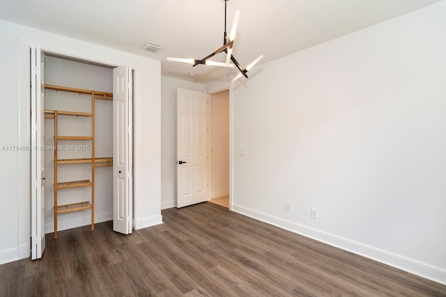 unfurnished bedroom featuring a closet, a notable chandelier, dark wood-type flooring, and baseboards