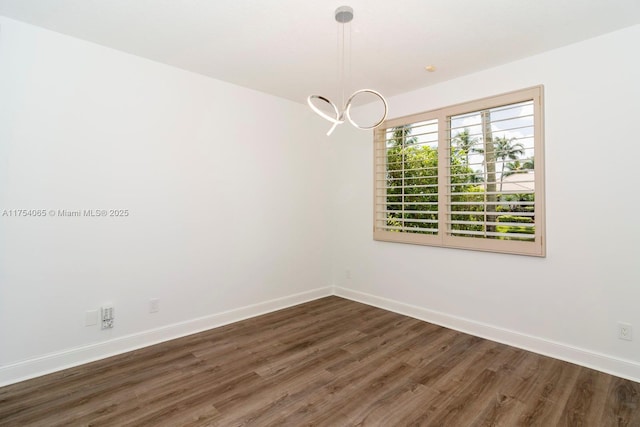 empty room featuring a notable chandelier, baseboards, and wood finished floors