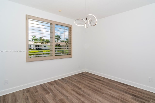 empty room with baseboards, a notable chandelier, and wood finished floors