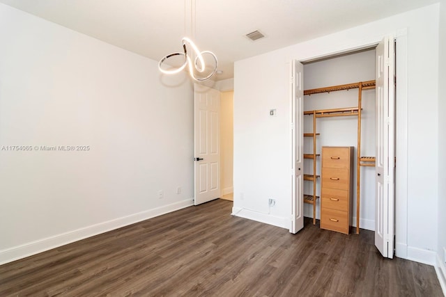 unfurnished bedroom featuring a closet, visible vents, a chandelier, baseboards, and dark wood-type flooring
