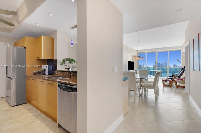 kitchen featuring stainless steel appliances, a sink, decorative backsplash, expansive windows, and dark stone countertops