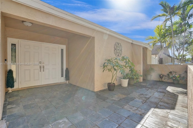 view of exterior entry with a patio area, fence, and stucco siding