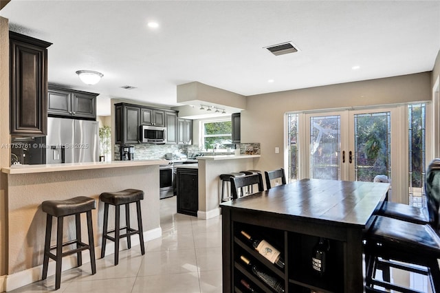 kitchen with visible vents, decorative backsplash, a peninsula, stainless steel appliances, and a kitchen bar