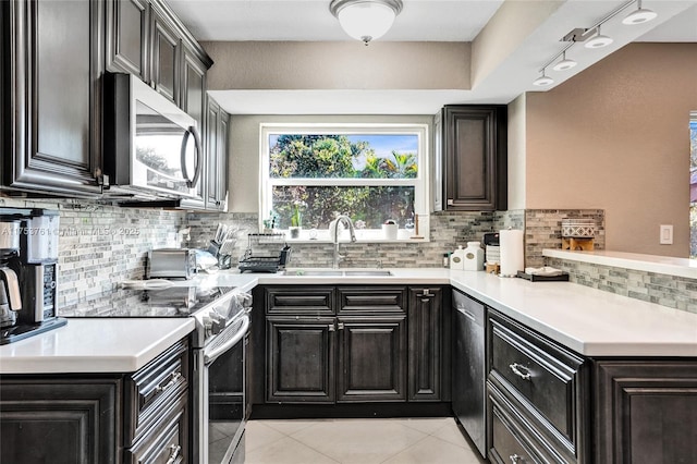 kitchen with light tile patterned floors, stainless steel appliances, light countertops, a sink, and a peninsula