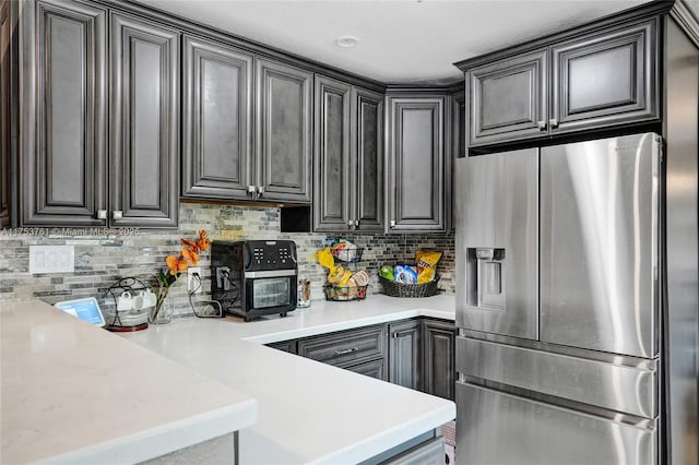 kitchen with light countertops, backsplash, stainless steel fridge with ice dispenser, and a peninsula