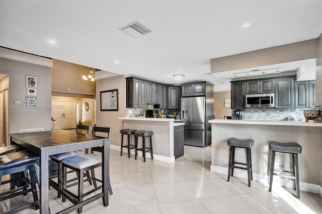 kitchen featuring a peninsula, visible vents, appliances with stainless steel finishes, tasteful backsplash, and a kitchen bar