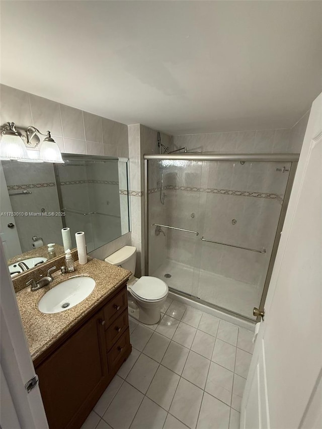 bathroom featuring toilet, tile patterned floors, vanity, a shower stall, and tile walls