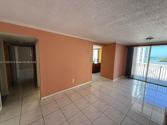 empty room with light tile patterned floors, a textured ceiling, baseboards, and crown molding