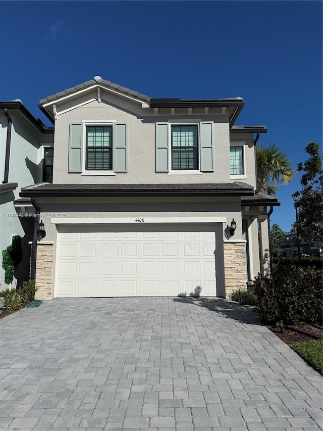 view of front of property with a garage, stone siding, decorative driveway, and stucco siding