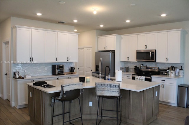 kitchen featuring a center island with sink, visible vents, appliances with stainless steel finishes, white cabinets, and wood finished floors