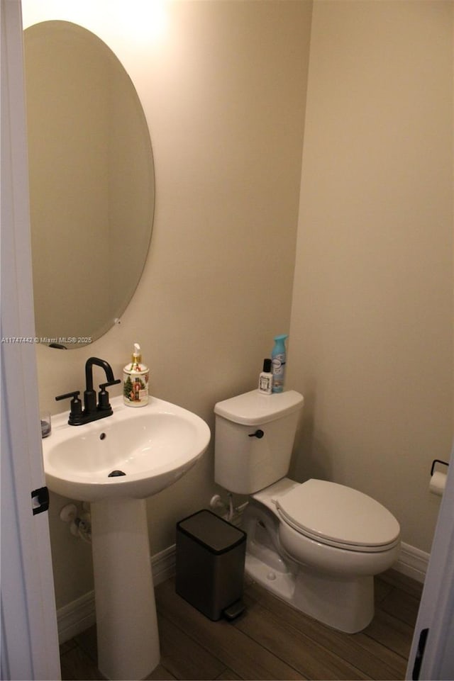 half bath with toilet, baseboards, and wood finished floors