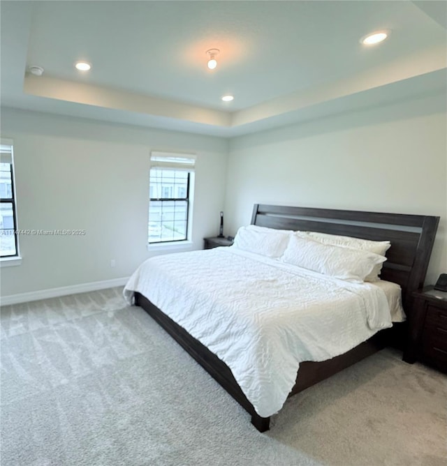 bedroom with a tray ceiling, multiple windows, and light colored carpet