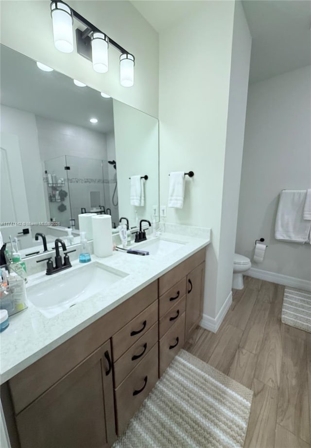 full bathroom with double vanity, a sink, a shower stall, and wood finished floors