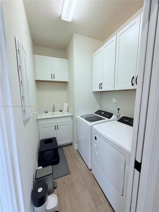 washroom featuring cabinet space, light wood-style flooring, a sink, a textured ceiling, and independent washer and dryer