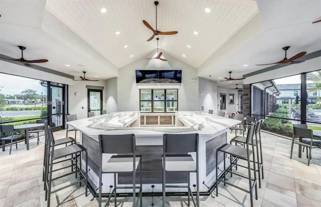 kitchen with open floor plan, a spacious island, lofted ceiling, and light stone countertops