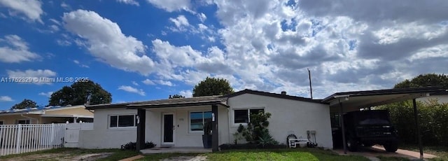 view of front of home with a carport, a gate, fence, and stucco siding