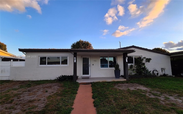 view of front of house featuring a porch, a front yard, fence, and stucco siding