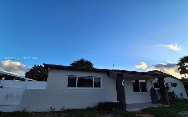 view of front of house featuring fence, a porch, and stucco siding