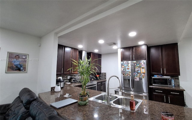 kitchen with a sink, dark brown cabinets, appliances with stainless steel finishes, tasteful backsplash, and dark stone countertops