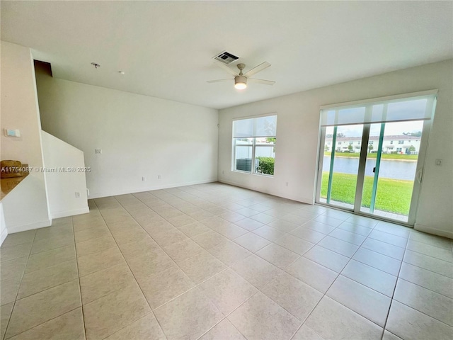 spare room featuring light tile patterned floors, visible vents, baseboards, ceiling fan, and a water view