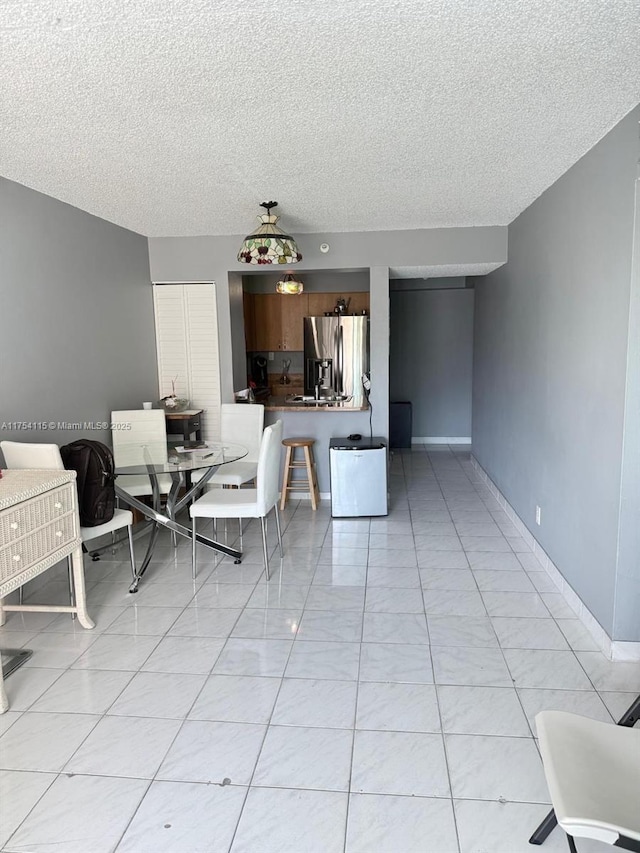 unfurnished living room featuring a textured ceiling, light tile patterned floors, and baseboards