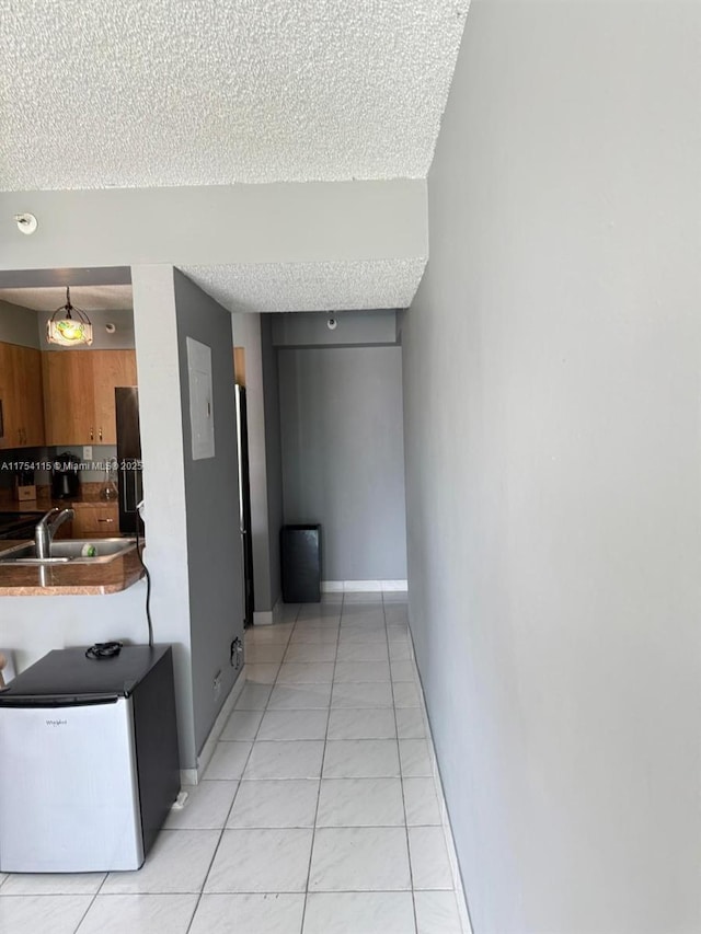 hallway featuring light tile patterned floors, a textured ceiling, a sink, and baseboards