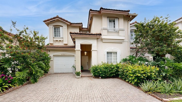 mediterranean / spanish-style home featuring decorative driveway, a tile roof, a balcony, and stucco siding